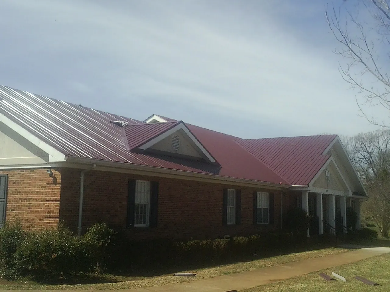 Red metal roof with gabled entries on a long brick building, from a Hail Damage Roof Repair job in Laurel