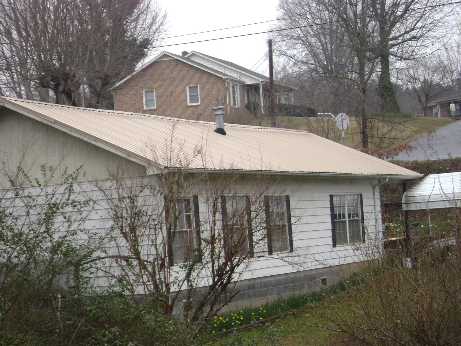 Tan metal roof on a white sided house set into a hillside — Commercial Roofing by Roofing Brothers in Laurel